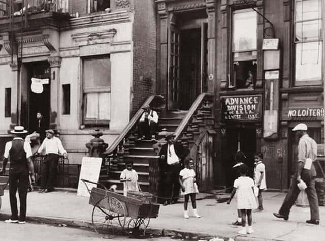 A black and white photograph of a street scene in Harlem, New York, during the 1930s, featuring pedestrians and buildings.