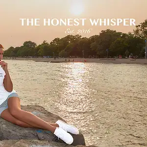 A woman wearing a white t-shirt with the humorous and vegan-friendly slogan "My soy milk frees all the cows from the yard." printed on it, sitting on a rock by the water.