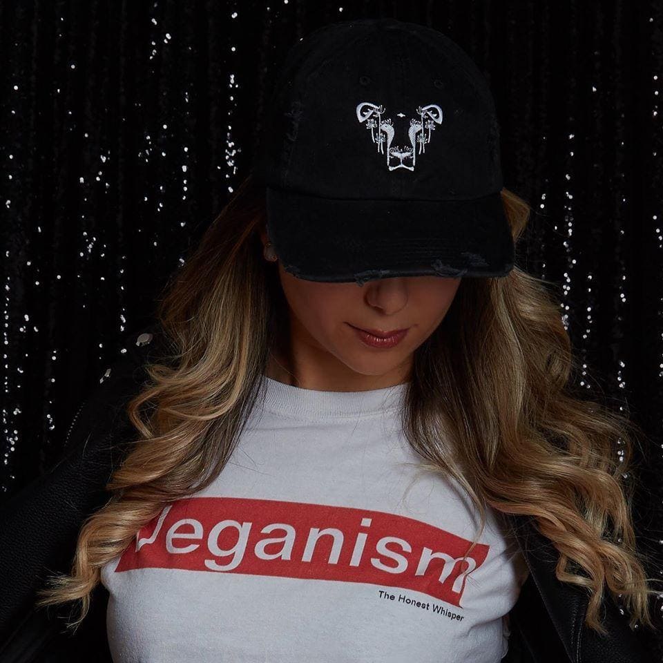 A woman proudly wears a "Veganism" t-shirt and a stylish Dandi Lion hat, both from The Honest Whisper, an ethical and sustainable fashion brand.