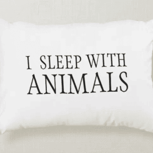 A white decorative pillow with the humorous text "I Sleep With Animals" printed on it.