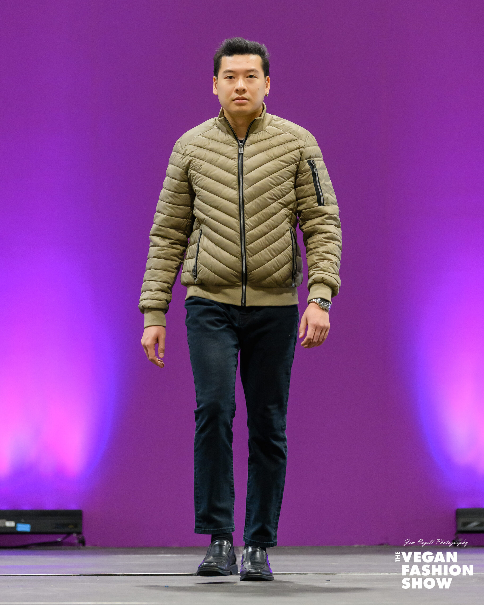 Jack-NOIZE-Alec-Puffer-Tan-Vegan-Fashion-Show Model Jack (Jackinguyen92) walks the runway in a tan/khaki, short-length, diamond-quilted puffer jacket (Alec style) by NOIZE, paired with dark blue jeans and black slip-on shoes, at The Vegan Fashion Show.