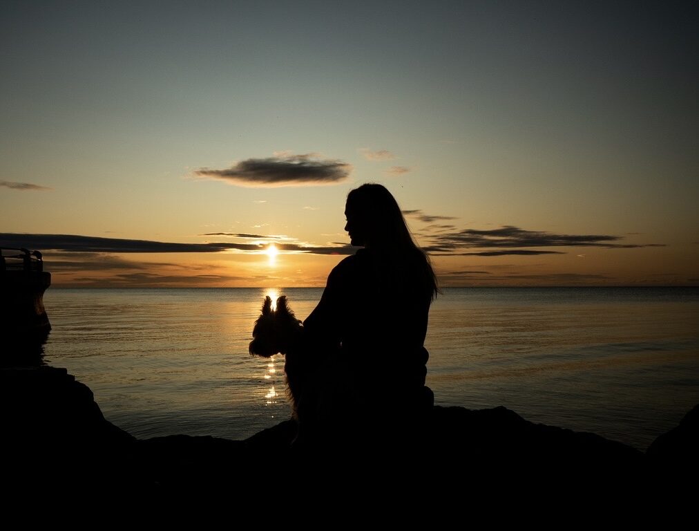 Sunset over water with a woman holding a cat, creating a peaceful and calming scene.
