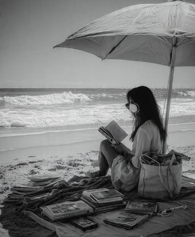 Woman reading a book on the beach under a large umbrella.