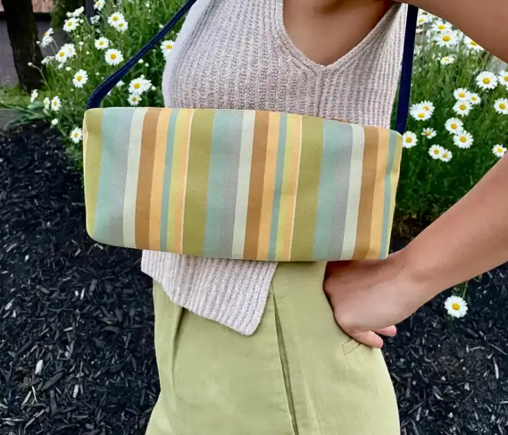 Woman holding a striped clutch bag outdoors with daisies in the background.