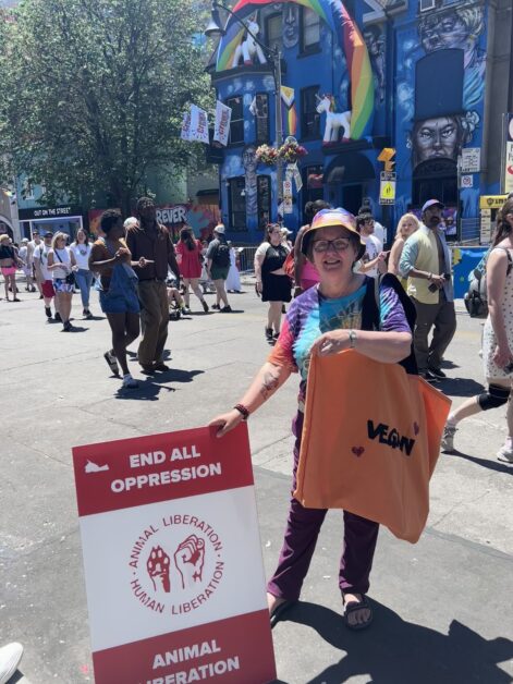 Woman holding animal rights sign at Pride parade in front of colourful building.