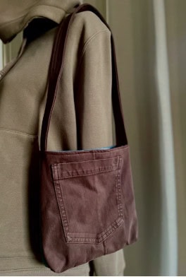 Upcycled brown denim fabric shoulder bag hanging on a beige coat.
